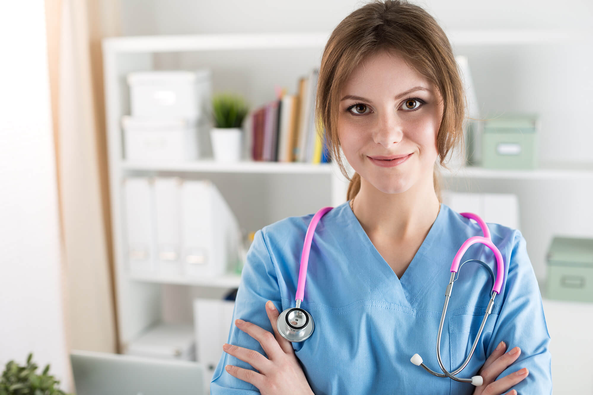Female nurse in blue scrubs with pink stethoscope